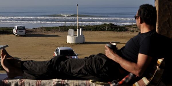 Ein Mann chillt auf der Terrasse im A Frame Surfcamp und beobachtet Wellen.